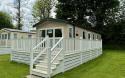 Outside View of a Caravan Holiday Home with a Decking area surrounded by Trees