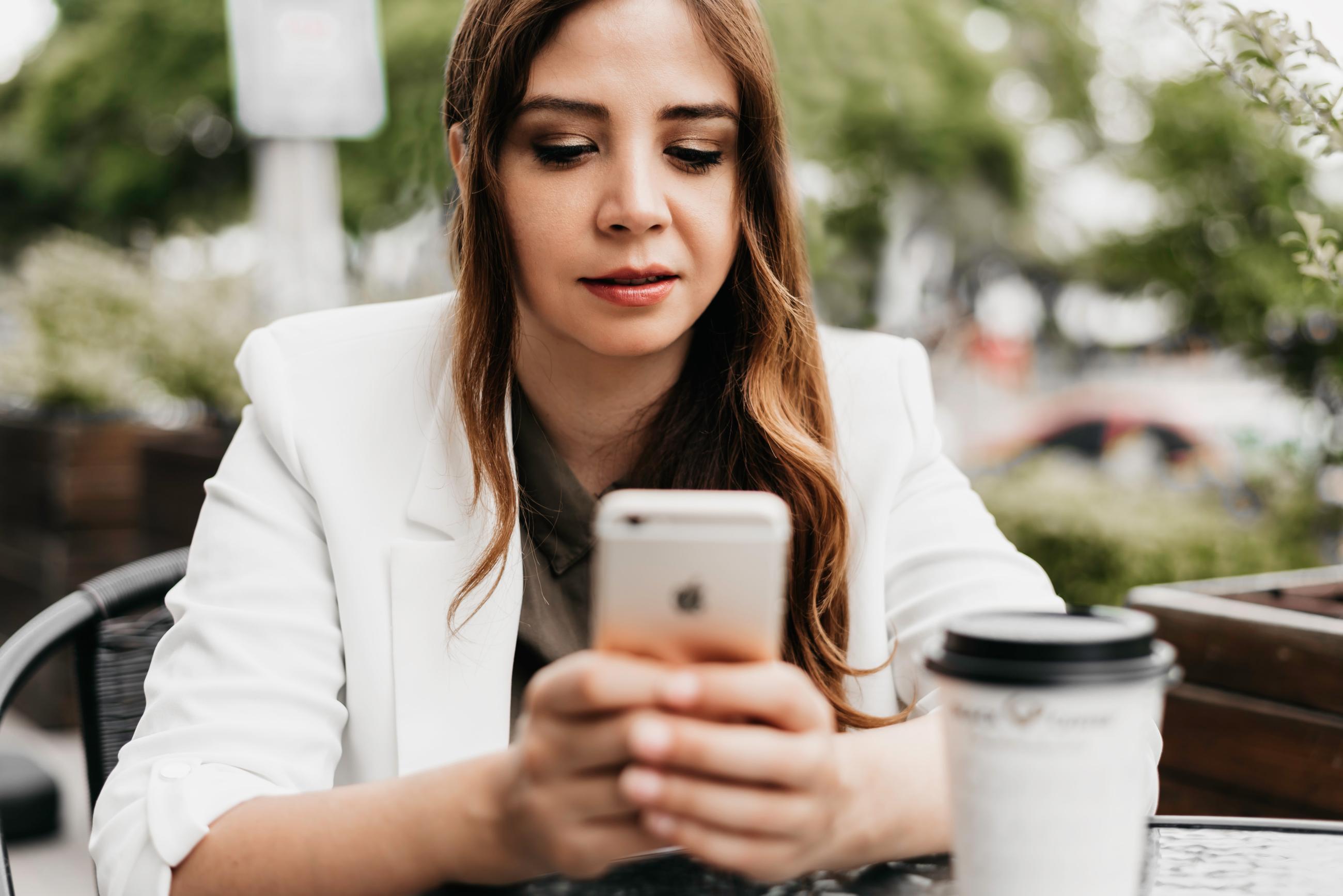 A Person Holding a Mobile Phone whilst drinking Coffee