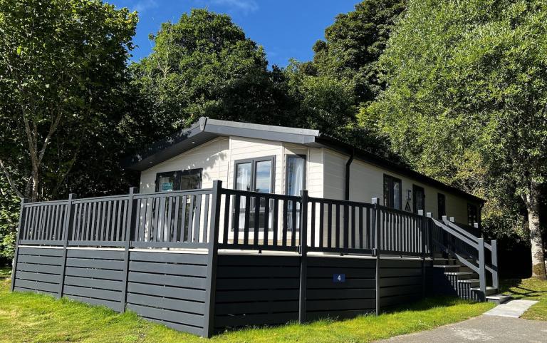 A Holiday Home with an exterior Decking area surrounded by Trees on a bright sunny day