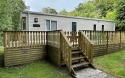 Outside View of a Caravan Holiday Home with a Decking area surrounded by Trees